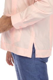 A close-up of a man wearing a light pink guayabera-style shirt with contrasting pink piping and blue pants, shown from the chest down against a white background.