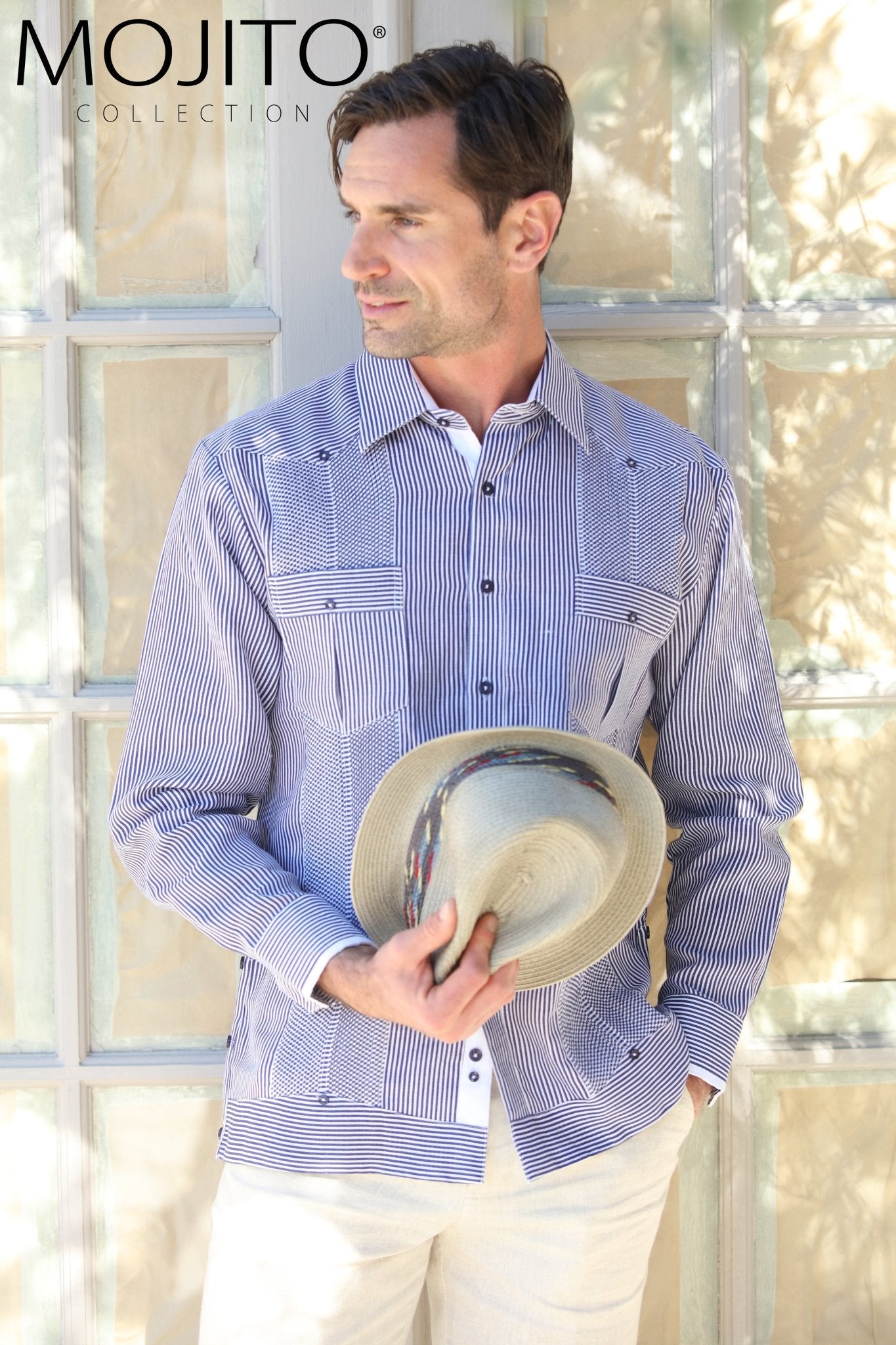 Man models the 100% Linen Contrast Panel Guayabera Shirt Long Sleeve in blue stripes, holding a fedora.
