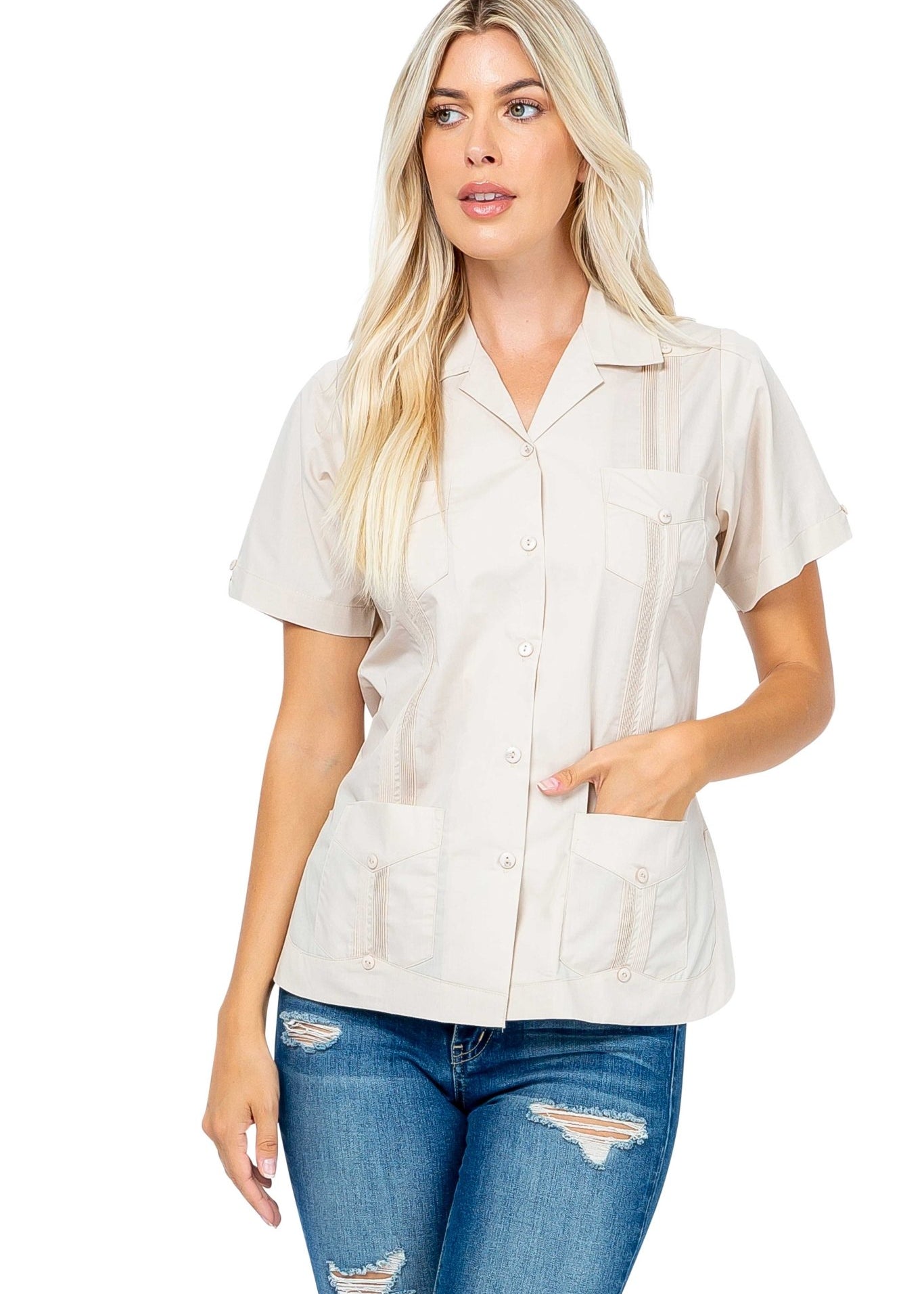 A woman models the beige Women's Short Sleeve Guayabera with 4 Pockets, wearing jeans and with one hand in a pocket.
