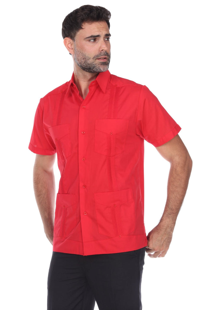 A man wearing a white short-sleeve guayabera-style button-up shirt with four front patch pockets, paired with black pants, photographed against a plain white studio background.