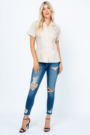 A blonde model wears a tan Women's Short Sleeve Guayabera with 4 Pockets, blue jeans, and black heels.