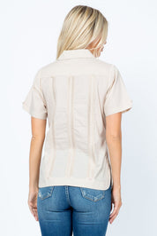 Back view of a woman wearing a tan Women's Short Sleeve Guayabera with vertical pleats and four pockets.