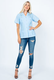 Model in a light blue Women's Short Sleeve Guayabera with 4 pockets, shown front-on, paired with jeans.